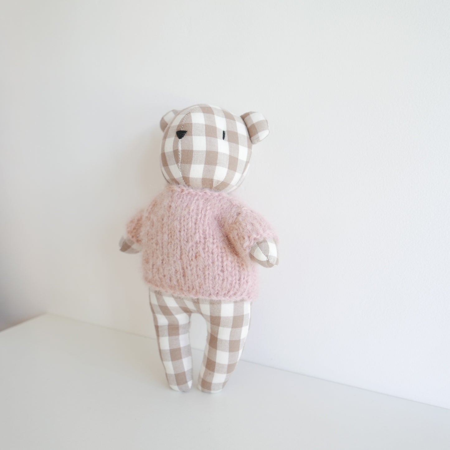 Stuffed teddy bear toy wearing a pink sweater and checkered pants on a white background