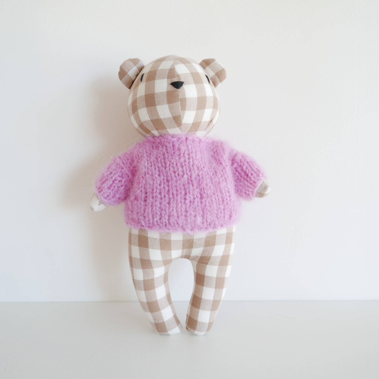 Teddy bear with a checkered hat and pink sweater on a white background