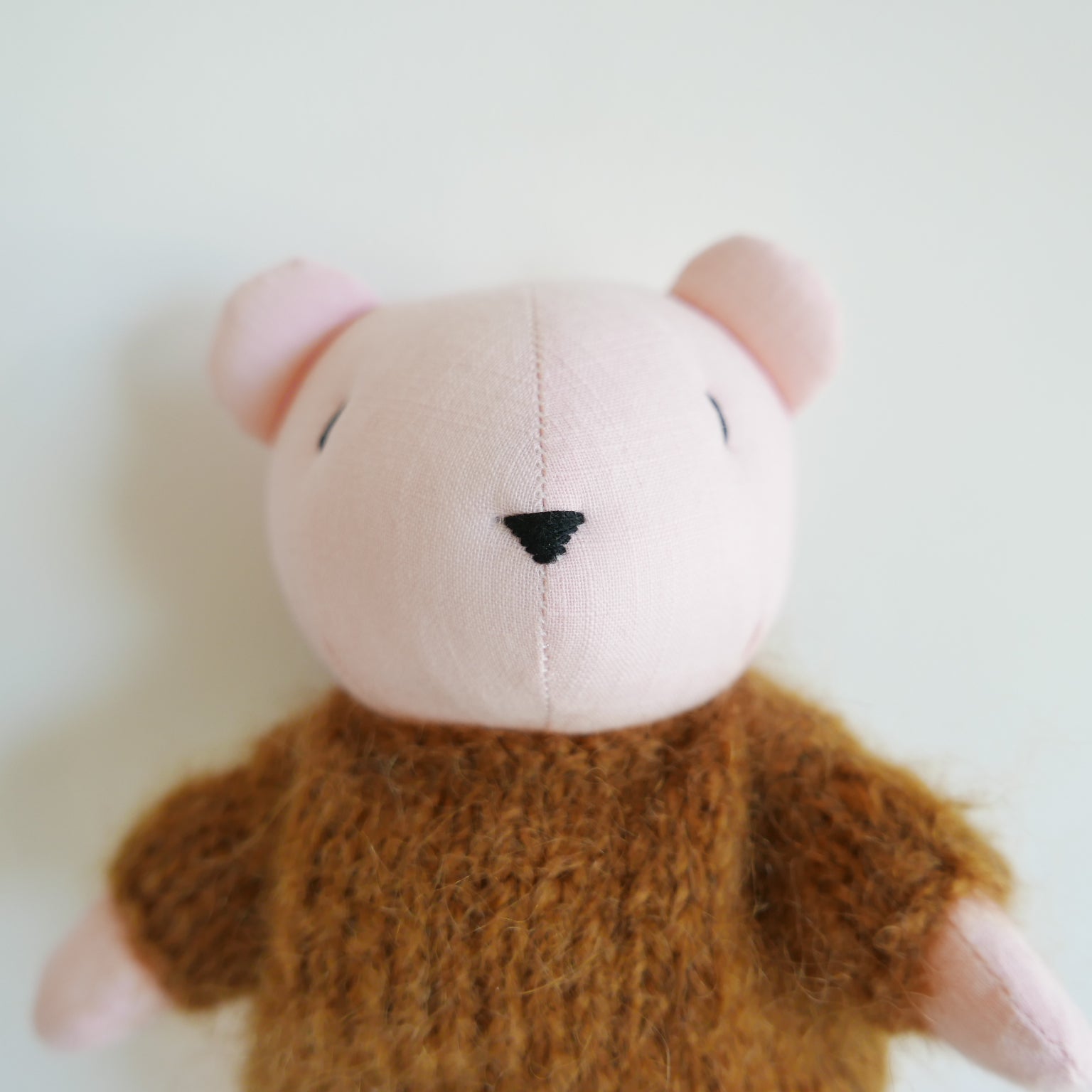 Small plush toy with a pink face and brown body on a white background