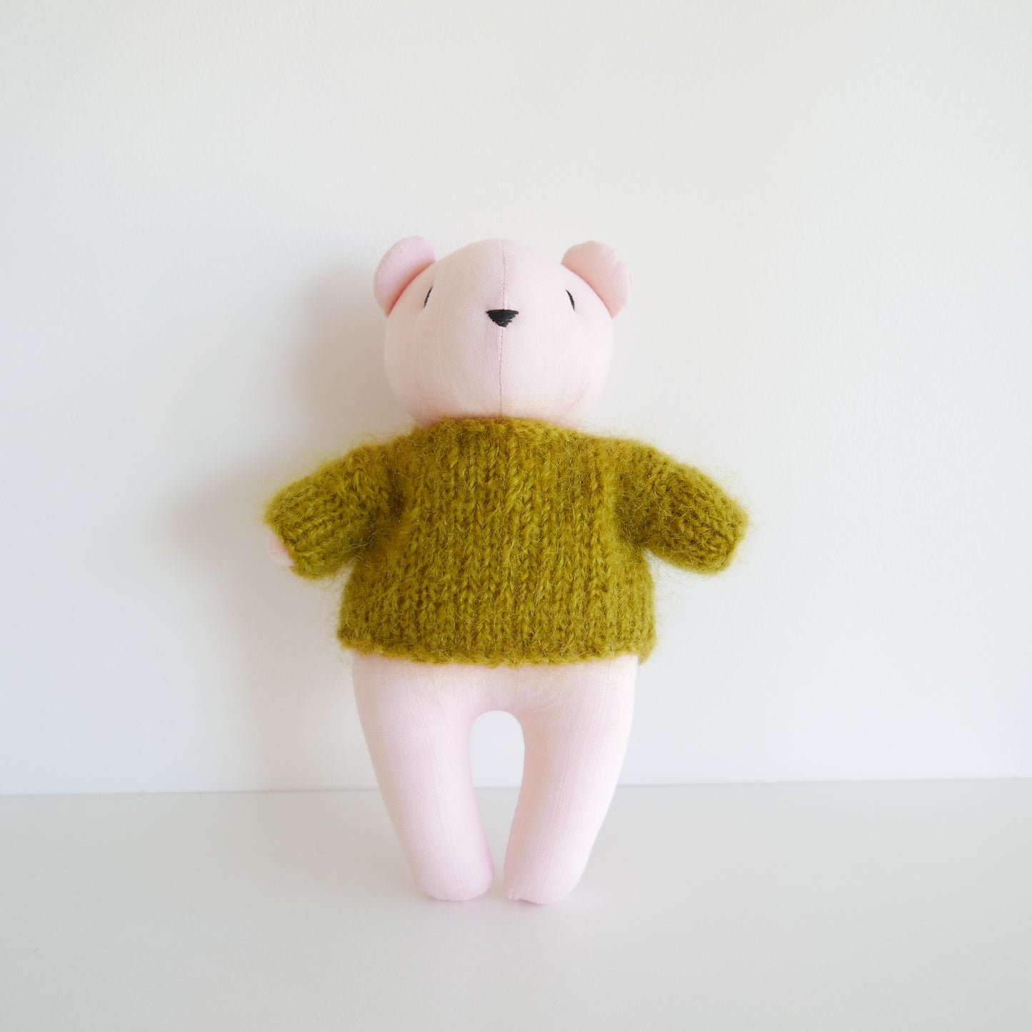 Small plush toy with a green knitted sweater on a white background