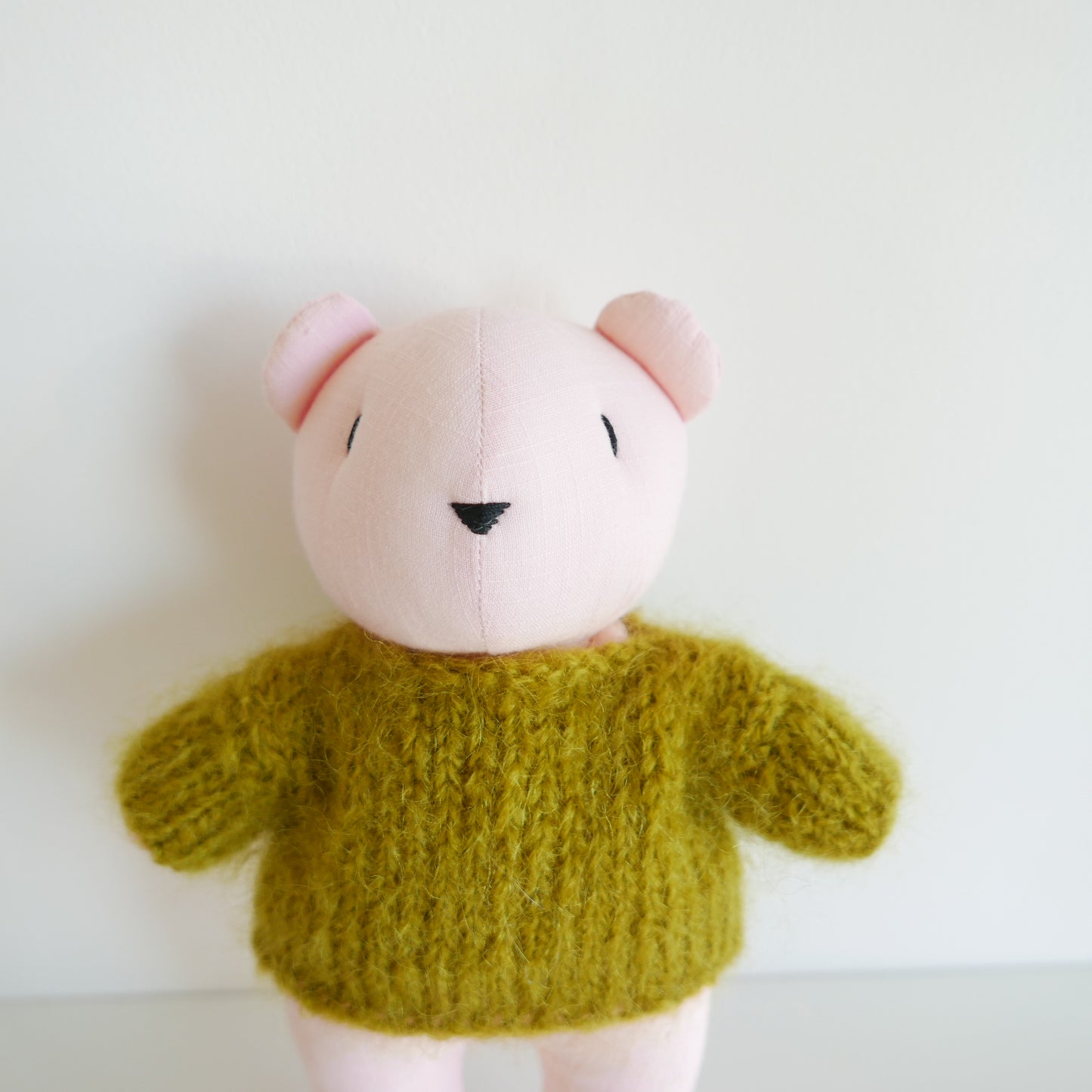 Stuffed animal toy with a green sweater on a white background