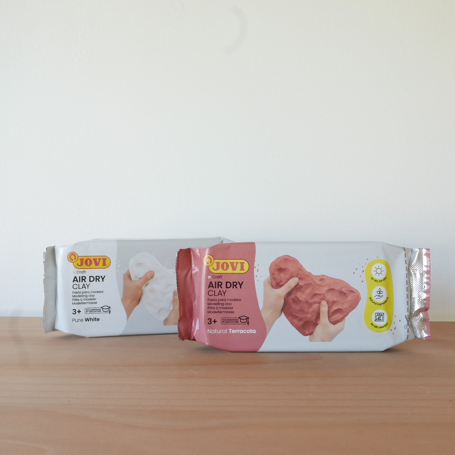 Two packages of JOVI air dry clay on a wooden surface with a white background