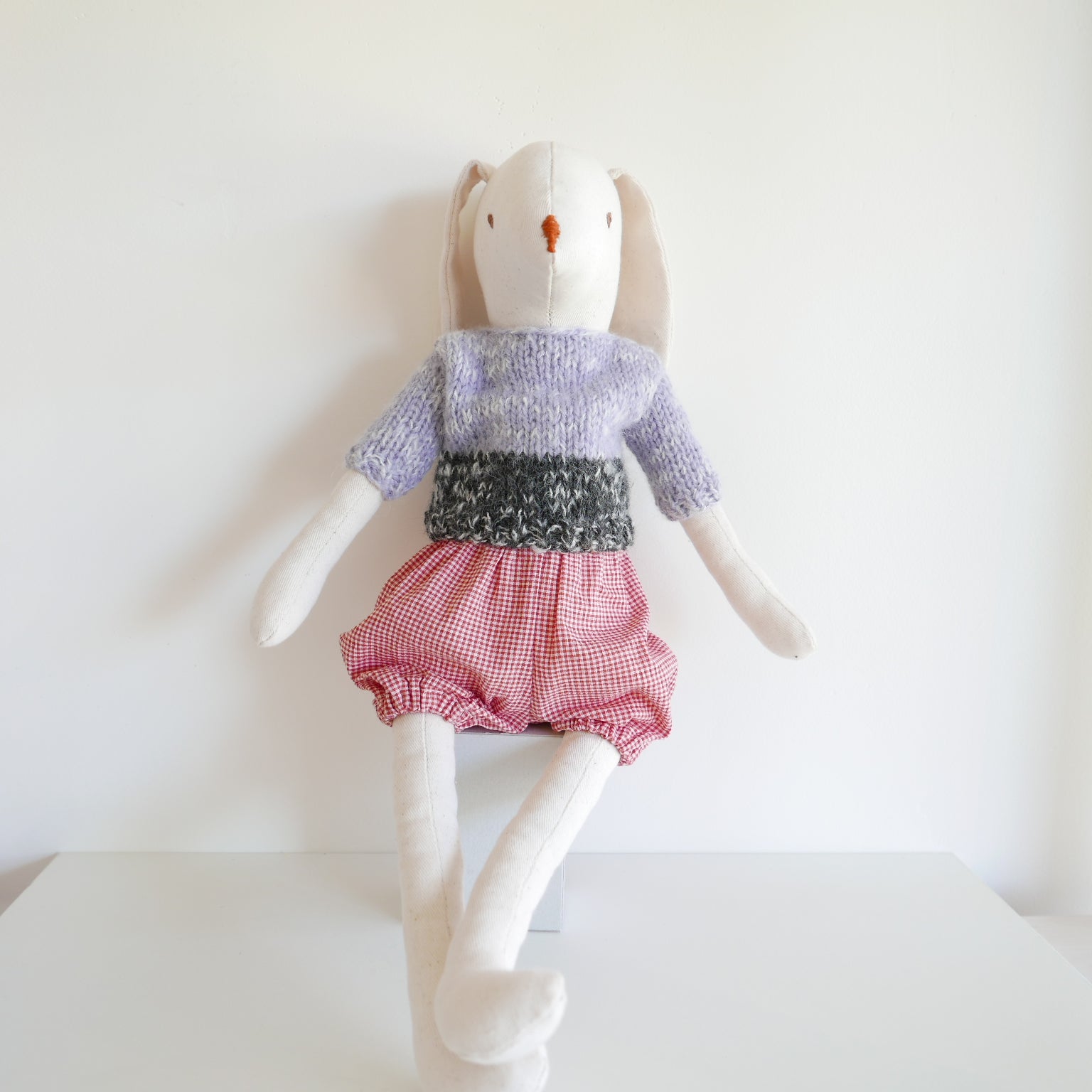 Stuffed toy rabbit wearing a sweater and checkered shorts on a white background