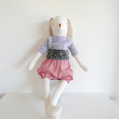 Stuffed toy rabbit wearing a sweater and checkered shorts on a white background
