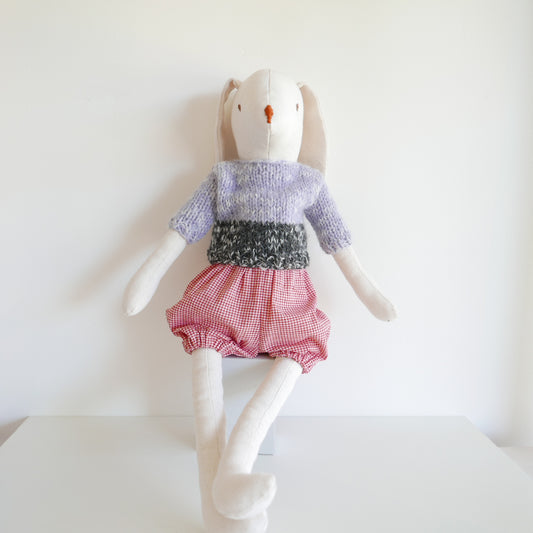 Stuffed toy rabbit wearing a sweater and checkered shorts on a white background