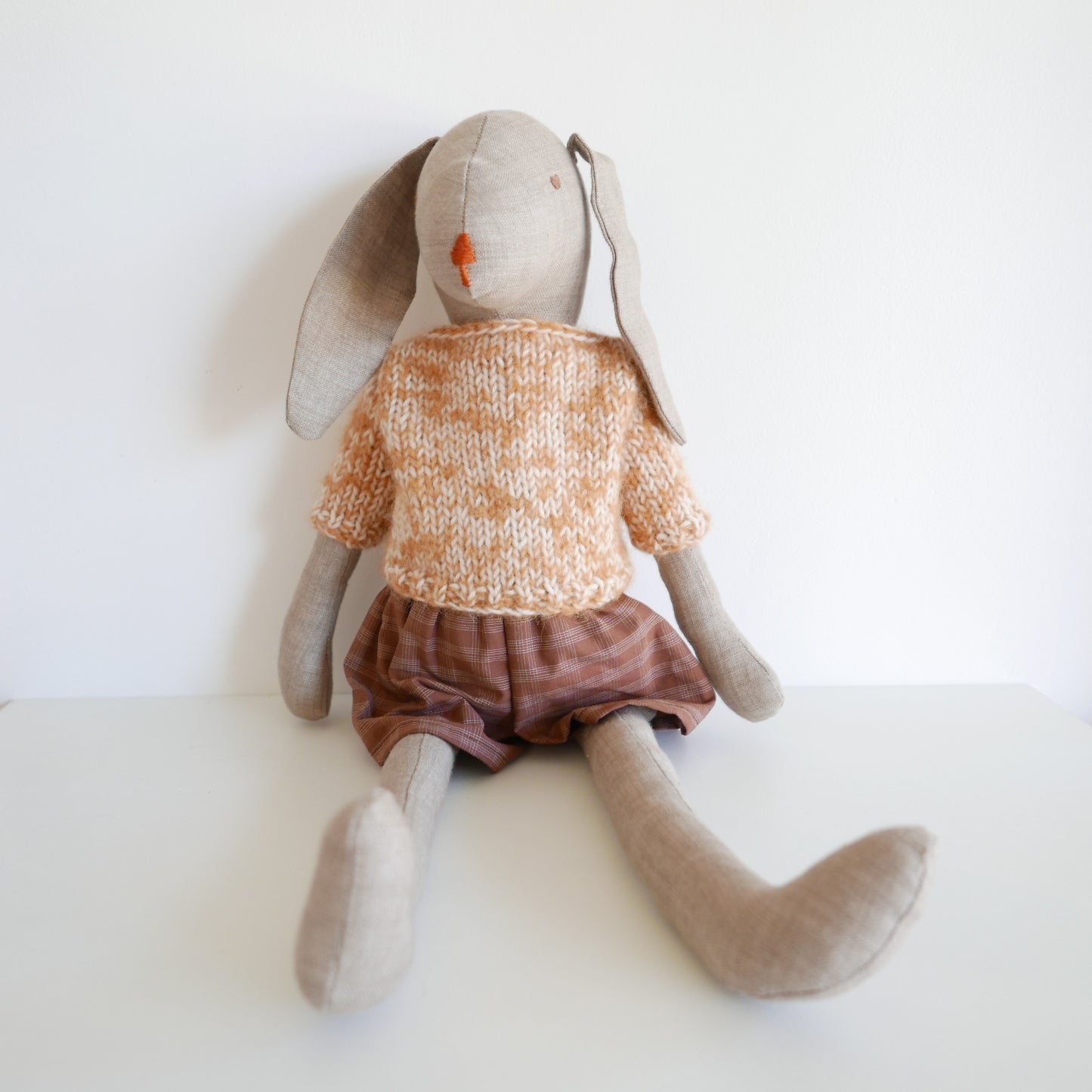 Stuffed animal rabbit wearing a knitted sweater and brown skirt on a white background