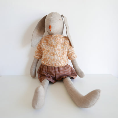 Stuffed animal rabbit wearing a knitted sweater and brown skirt on a white background