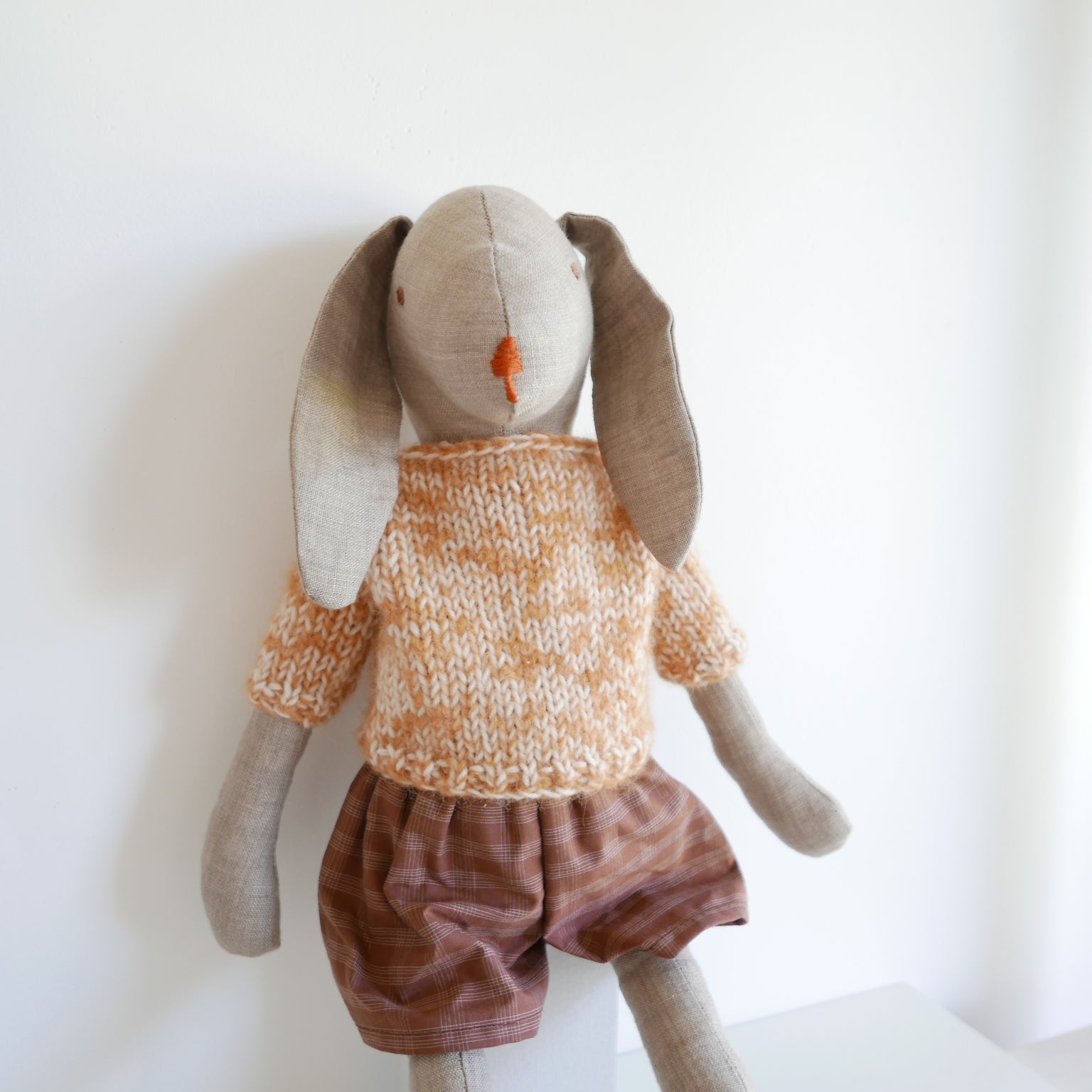 Stuffed toy rabbit wearing an orange sweater and brown shorts on a white background