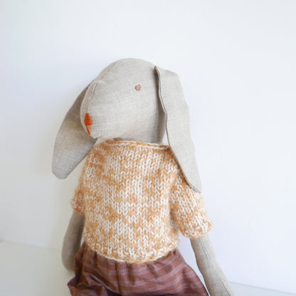 Toy rabbit wearing a knitted sweater on a white background